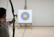Un archer de dos, arc tendu, silhouette en contre-jour dans une salle claire.webp