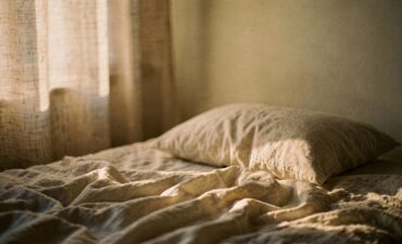 Lit défait et draps de lin clairs éclairés par la première lumière du jour à travers un rideau